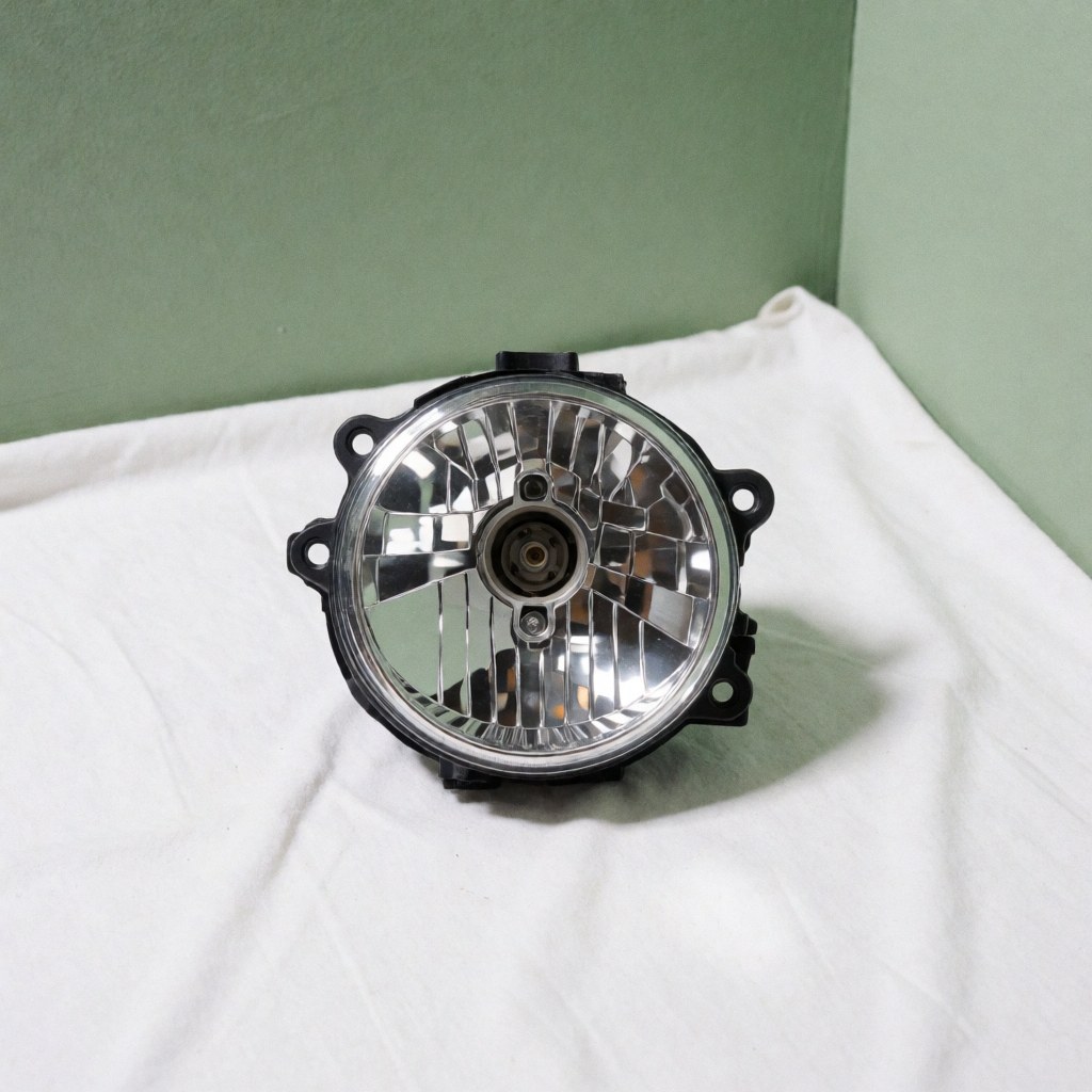 Un phare de voiture neuf et propre posé sur un tissu blanc avec un mur vert pâle en arrière-plan pour illustrer le recyclage automobile.