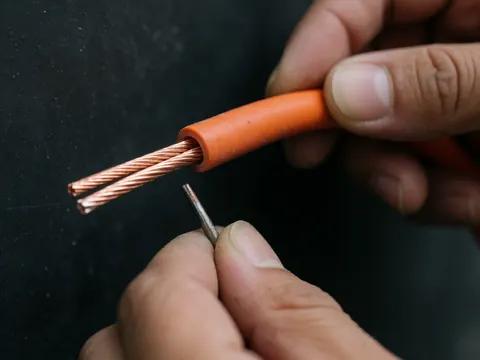 Câble THW-2 à isolation orange et conducteur en cuivre brillant, tenu avec précision par une main sur fond sombre professionnel.