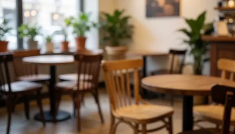 Fond de café avec tables rondes, chaises en bois, plantes vertes et lumière chaleureuse, idéal pour ajouter du texte.