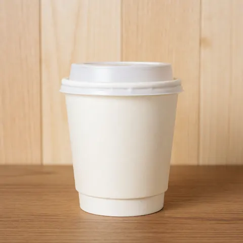 Une tasse de café jetable avec un couvercle blanc posée sur une table en bois, devant un fond de panneaux de bois clair, sous un éclairage lumineux et propre.