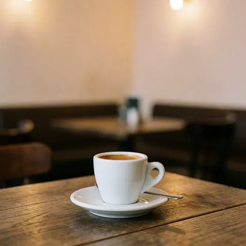 Tasse d'espresso blanc posée sur une assiette avec une cuillère, sur une table en bois rustique dans un café aux murs beige et à la lumière chaude