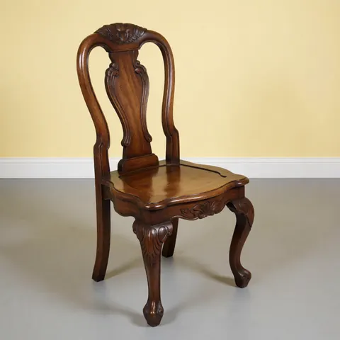 Chaise en bois ancien restaurée avec un fini brillant et des détails sculptés, posée sur un sol gris devant un mur jaune pâle.