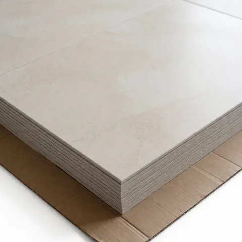 Empilement de carreaux de sol beige à texture pierre posés sur du carton protecteur, éclairage professionnel pour catalogue produit.