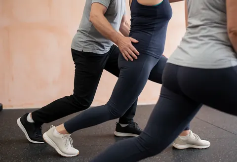 Un coach de crossfit corrige la posture de son client lors d'un exercice de fente dans un gymnastique lumineux aux murs de terre cuite.