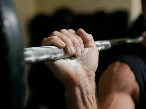 Gros plan d'une main adulte recouverte de poudre blanche agrippant fermement une barre de musculation sur fond sombre et flou, mettant en valeur la texture réaliste.