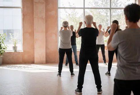 Des adultes suivent un cours de boxe dans une salle de sport baignée de lumière naturelle.