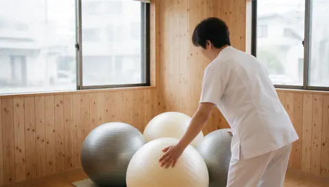 Un professionnel en tenue blanche règle trois ballons de stabilité dans un cabinet aux murs boisés et à la lumière naturelle.