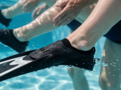 Détail du pied d'un adulte portant une palm noir, nageant dans une piscine avec des bulles et une lumière naturelle, illustrant la technique de natation.