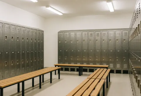 Vestiaire propre et ordonné équipé de casiers métalliques et de bancs en bois, éclairé par des néons, idéal pour les pratiquants d'arts martiaux.
