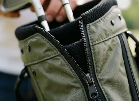 Fermeture éclair ouverte d'un sac de golf révélant la texture du tissu et les tiges des clubs, éclairée par une lumière naturelle douce.