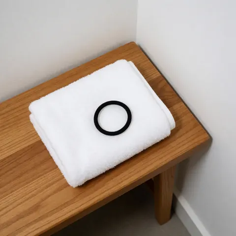 Serviette blanche pliée et bandeau élastique noir posés sur un banc en bois clair, composition minimaliste évoquant le soin post-cours de danse.