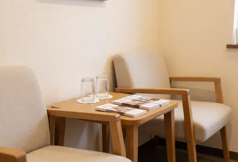 Réception de massage cervical avec chaises confortables, table en bois avec eau et brochures, murs beige, ambiance calme et accueillante pour les clients.