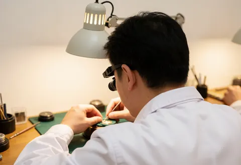 Un horloger professionnel ajuste minutieusement le mécanisme d'une montre sous l'éclairage d'une lampe dans son atelier.