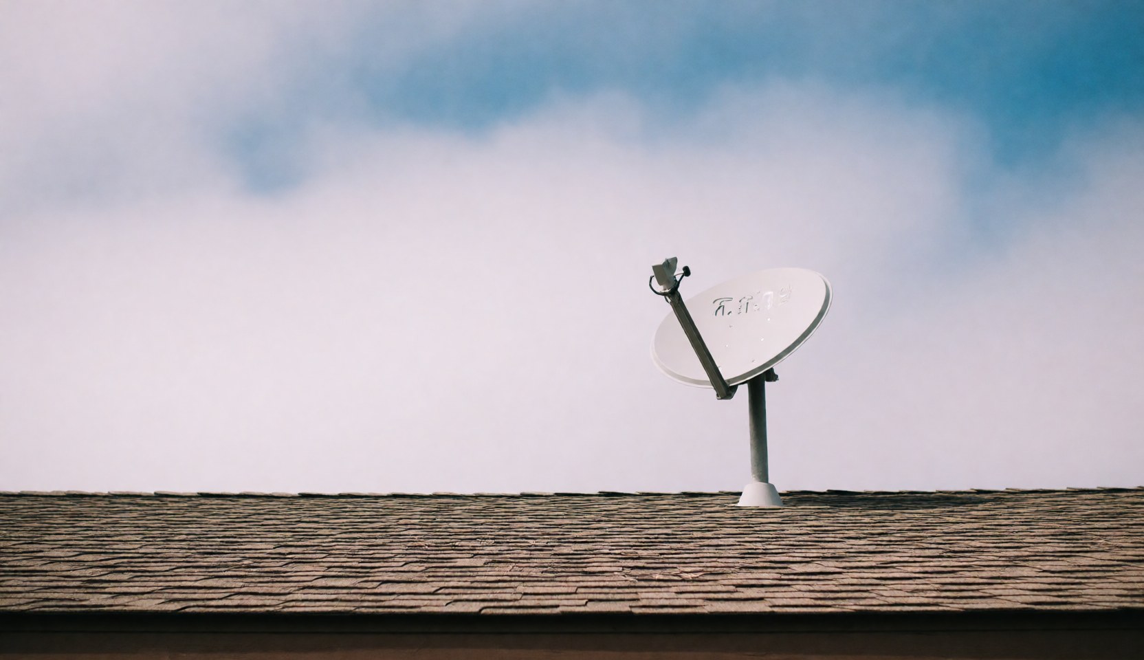 Une antenne satellite blanche est fixée sur un toit en tuiles, se détachant contre un ciel bleu parsemé de nuages blancs.