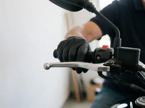 Gros plan d'une main portant un gant noir réglant le levier de frein dans un atelier avec des outils en arrière-plan flou.
