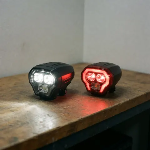 Un phare blanc et un phare rouge de vélo sont allumés sur une surface en bois texturée, émettant une lumière vive qui met en valeur les détails des composants.
