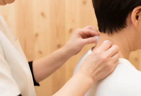 Un thérapeute pratique un massage avec des ventouses sur le cou d'un client, mains et outils visibles, fond en bois naturel, ambiance relaxante.