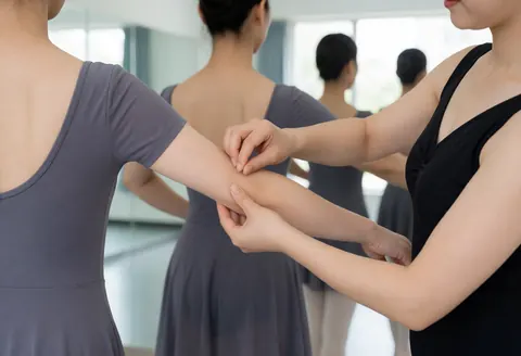 Une instructrice de danse corrige la posture du bras d'une élève dans un studio lumineux avec des miroirs.