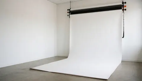 Studio photo vide avec fond blanc tendu au plafond, sol en béton poli et éclairage naturel doux, prêt pour des portraits professionnels.