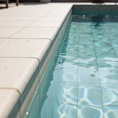 Vue d'une piscine extérieure aux eaux claires bordée d'un deck en carreaux, offrant un cadre moderne et propre pour se détendre au soleil.