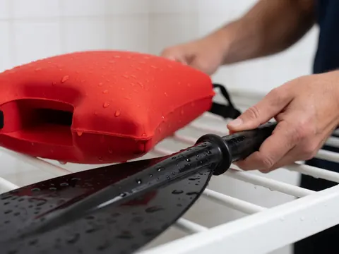 Gros plan d'une main adulte tenant une pelle noire et un flotteur rouge sur une grille blanche humide dans une piscine publique.