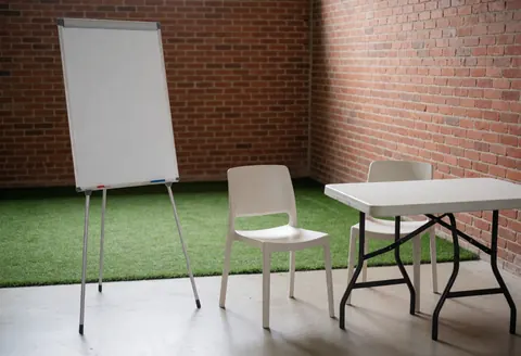 Espace de travail pour entraîneurs avec tableau blanc, chaises et table posés sur une pelouse synthétique devant un mur en briques.