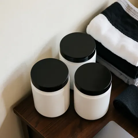 Trois tubes blancs de compléments alimentaires avec des couvercles noirs posés sur une table en bois foncé, accompagnés de serviettes de sport pliées dans un contexte d'entraînement.