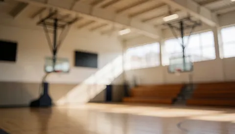 Arrière-plan flou d'un gymnase de basket-ball avec paniers, bancs et lumière naturelle, idéal pour ajouter du texte.