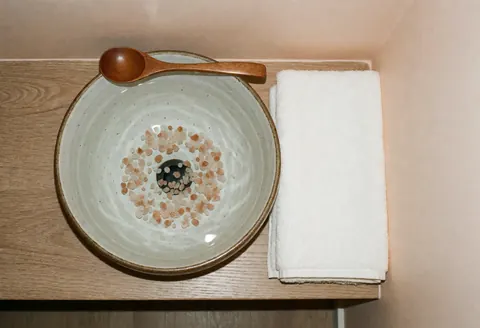 Bol en céramique contenant du sel rose et une cuillère en bois, posé à côté d'une serviette blanche dans un contexte de bain de pieds pour la réflexologie.