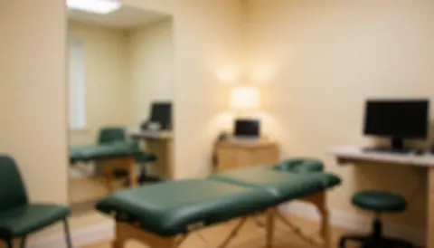 Intérieur d'une salle de traitement en physiothérapie comportant des lits verts, un miroir, des ordinateurs et des murs beige dans une ambiance calme et professionnelle.
