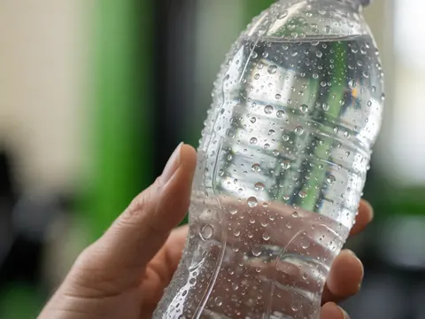 Gros plan sur une main tenant une bouteille d'eau avec des gouttes de condensation, évoquant l'hydratation et la fraîcheur lors d'un entraînement en salle.