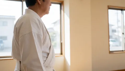 Adulte en tenue blanche d'arts martiaux de profil dans un dojo beige lumineux, idéal pour site web d'instructeur.