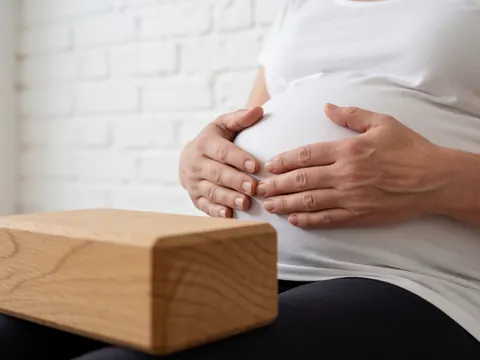 Mains reposant sur le ventre, bloc de yoga en bois au premier plan, mur de briques blanches et posture de détente.