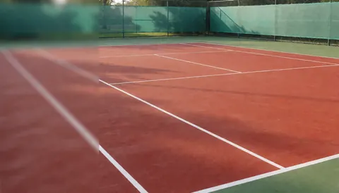 Détail d'un court de tennis en terre battue rouge marqué de lignes blanches, entouré d'une clôture verte, servant de fond neutre pour un texte promotionnel lié au sport.