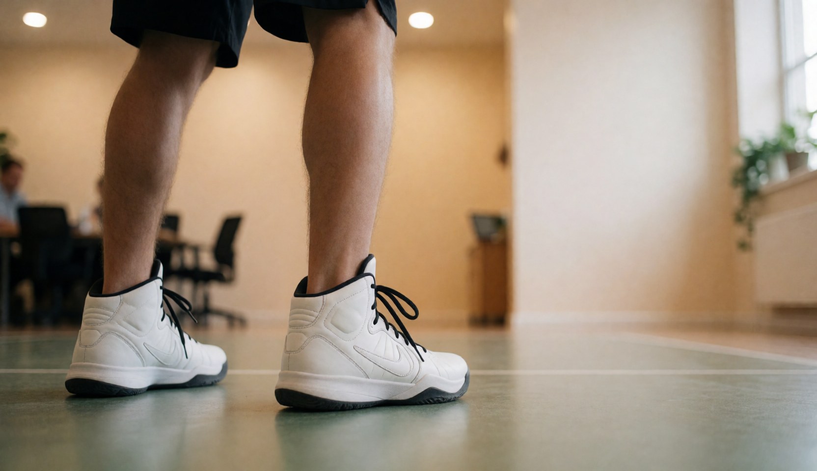 Vue arrière de chaussures de basketball blanches à lacets noirs posées sur un sol de gymnase beige, idéal pour une page d'accueil web.