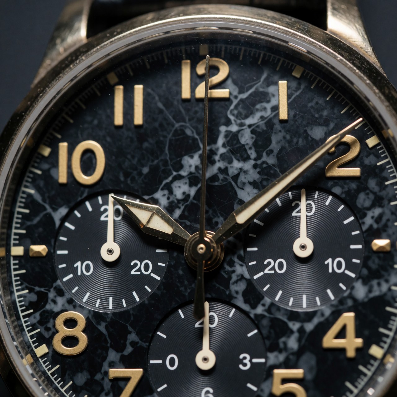 Fermoir de montre-bracelet avec cadran en marbre noir et chiffres dorés, montrant les aiguilles et le sous-cadran chronographe en détail pour photographe produit.