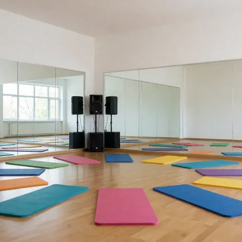 Vue d'un espace de fitness moderne comprenant des tapis d'exercice multicolores disposés sur le sol, des murs entièrement recouverts de miroirs et des haut-parleurs installés pour les cours.