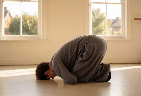 Un instructeur de danse réalise un mouvement sur un plancher en bois dans un studio baigné de lumière naturelle avec des murs clairs.