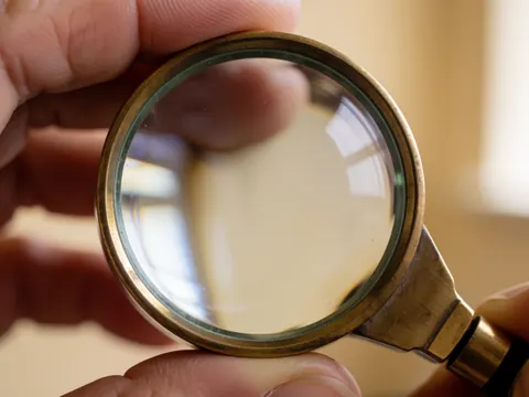 Loupe de bijoutier à cadre en bronze tenue par des mains, sur fond flou de atelier, idéale pour les détails techniques de la reloqueterie.