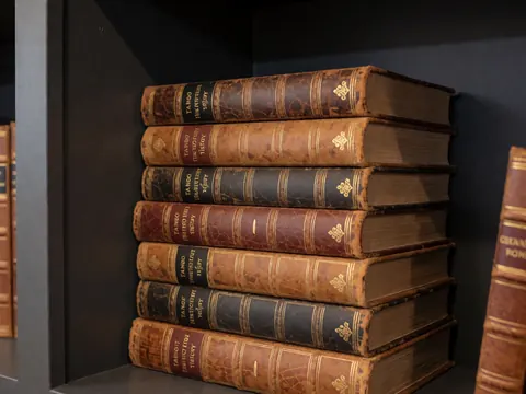 Une pile de livres anciens traitant de l'histoire du tango posée sur une étagère en bois avec des murs gris charbon, éclairage chaleureux et professionnel.