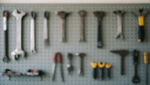 Fond flou d'outils suspendus sur un panneau mural gris, idéal pour illustrer les services de maintenance et de réparation.
