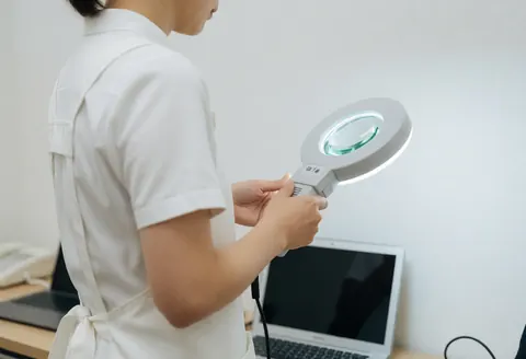 Un professionnel en blouse blanche examine la peau à l'aide d'une loupe dans un environnement clinique propre pour le traitement de l'acné.