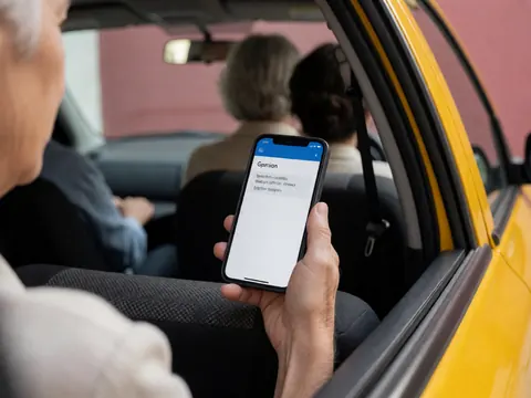 Vue rapprochée d'une main tenant un smartphone à l'intérieur d'un taxi jaune avec un mur rose en arrière-plan pour illustrer le service de traduction.