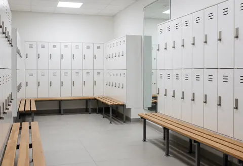 Vestiaire propre avec casiers blancs, bancs en bois et miroirs, idéal pour un gymnase ou un centre de boxe.