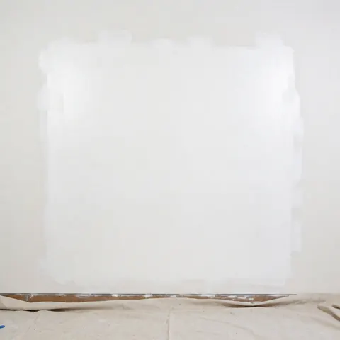 Détail d'un mur blanc réparé et lisse, prêt pour la peinture, avec une bâche de protection au sol, adapté aux professionnels de la rénovation.