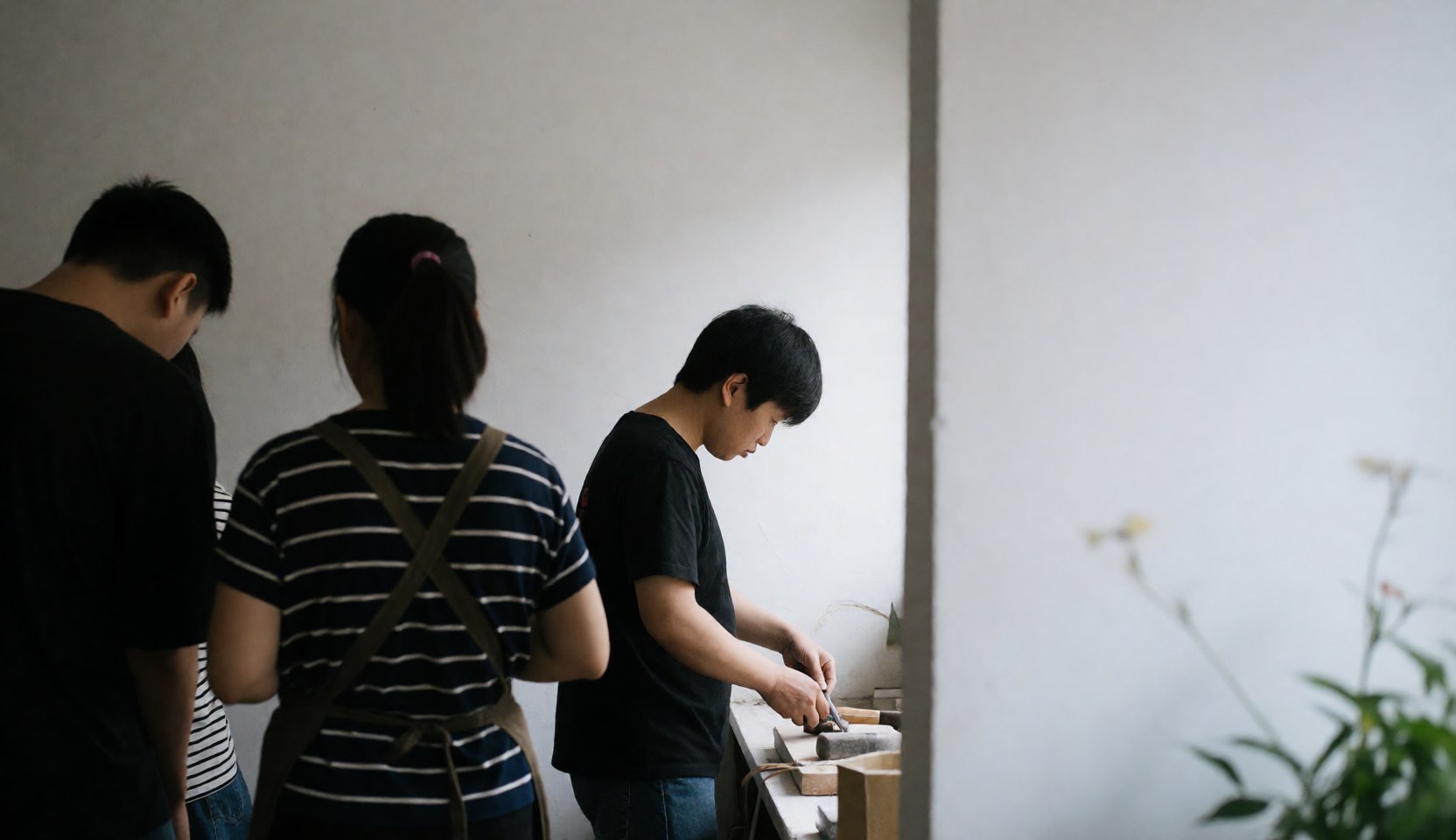 Trois individus regardent un artisan utiliser des outils dans un atelier de menuiserie aux murs blancs.