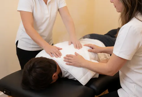 Deux praticiens réalisent un massage à la vapeur sur le dos d'un client allongé sur une table de soin dans un cadre professionnel.