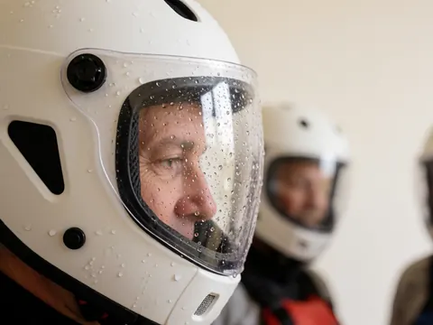 Un casque de sécurité blanc présentant des gouttelettes d'eau sur son visor embué, posé contre un mur blanc dans un environnement intérieur.
