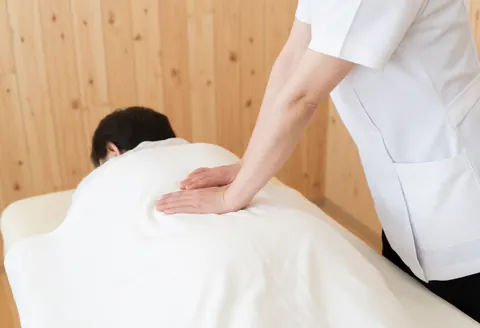Un thérapeute en uniforme blanc applique un massage professionnel sur le dos d'un client, utilisant une serviette blanche dans un espace de soins.