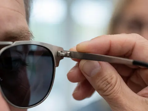 Main ajustant la charnière de lunettes de soleil métalliques à verres courbés sur fond flou, mettant en valeur un accessoire optique de haute qualité.